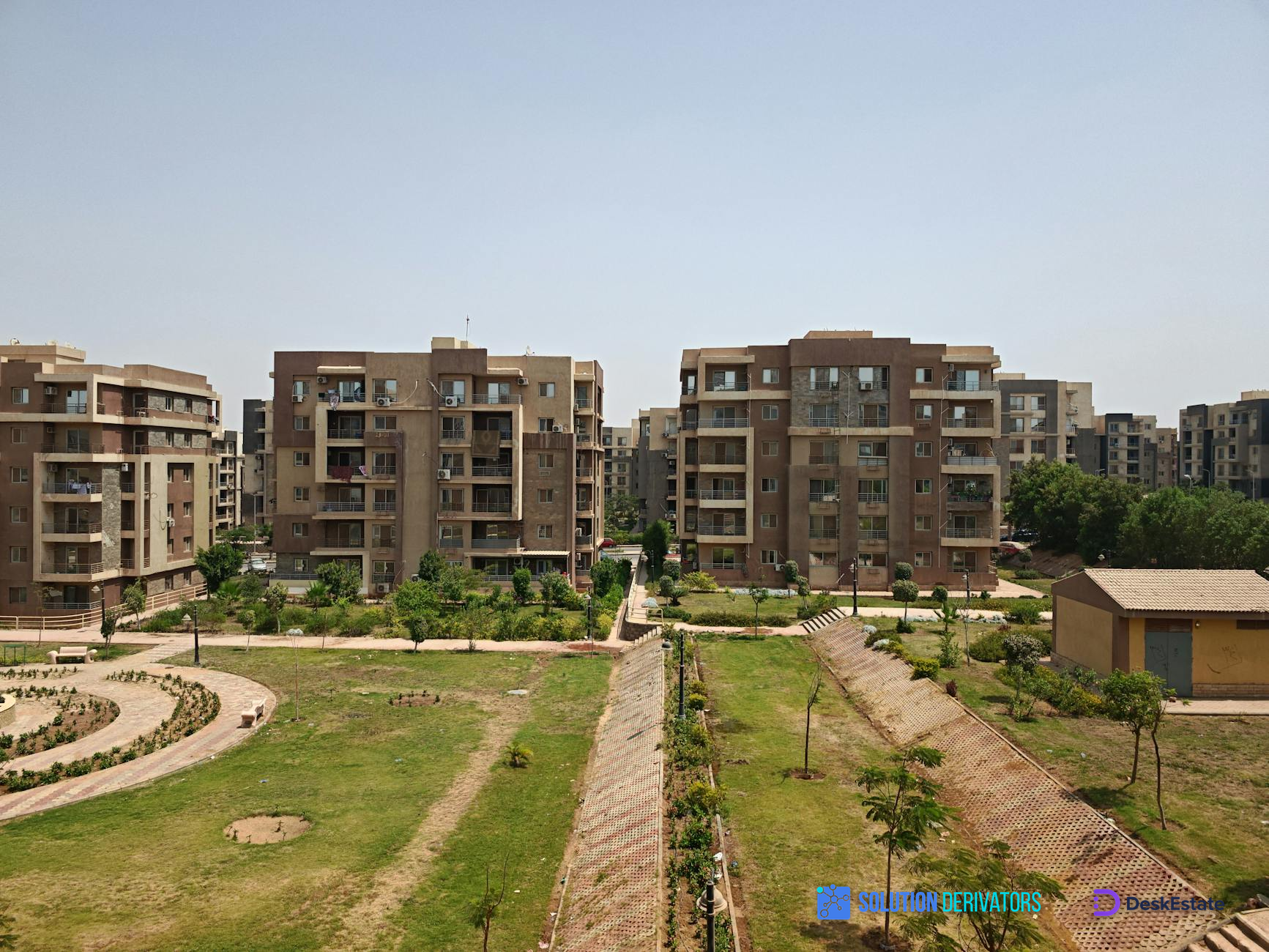 Aerial view of modern apartment buildings surrounded by lush greenery on a sunny day.