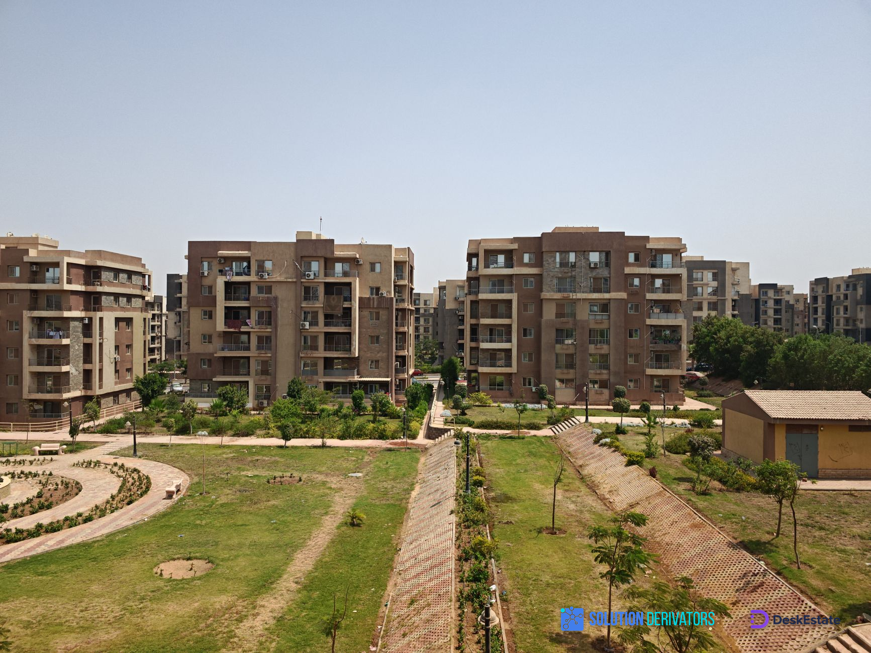 Aerial view of modern apartment buildings surrounded by lush greenery on a sunny day.